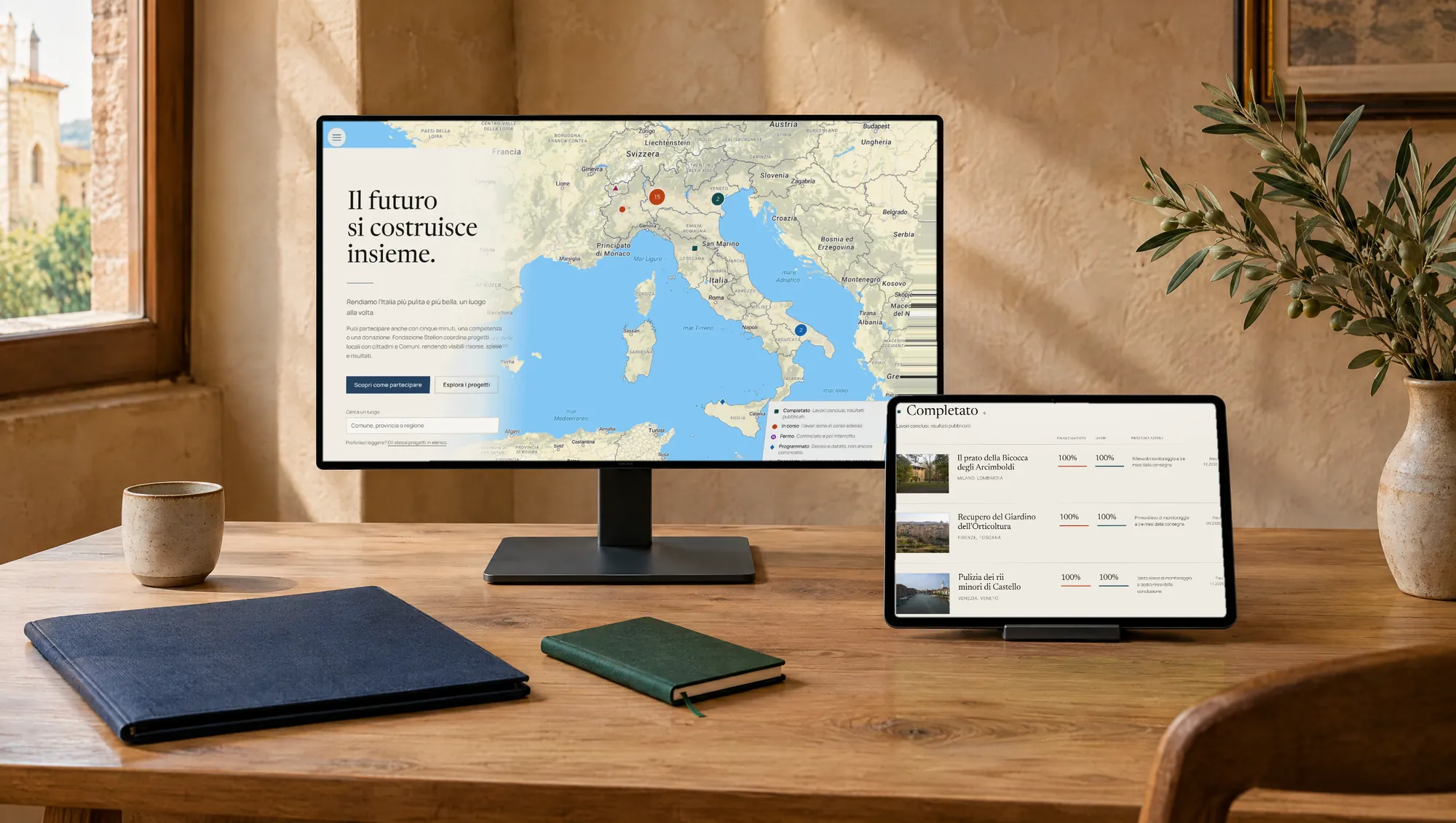 Il sito di Fondazione Stelion su monitor e tablet, su un tavolo di legno in una stanza dai muri caldi