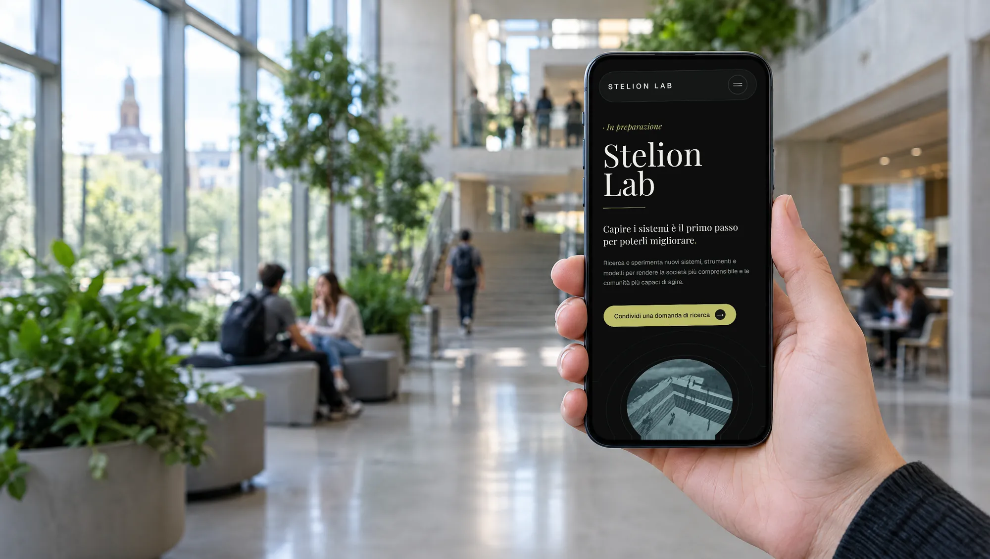 Il sito di Stelion Lab su un telefono tenuto in mano nell’atrio di un’università